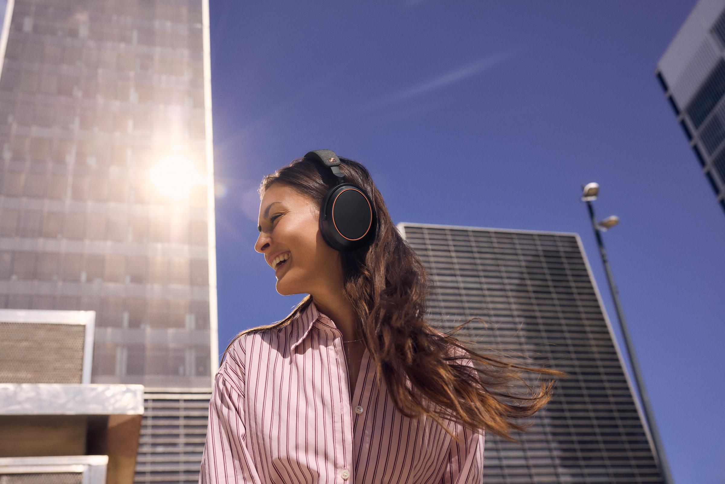 Sennheiser MOMENTUM 4 Wireless Copper City Mood Shot, Woman Wearing Headphones in Urban Setting